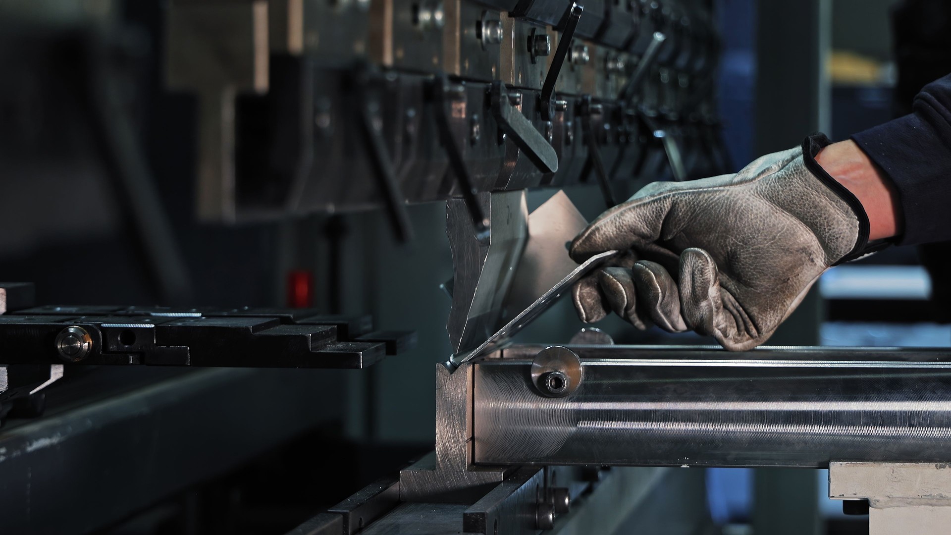 Sheet metal bending on CNC machine. Gloved worker bending a metal sheet using a CNC press brake in an industrial setting focused on precision manufacturing.